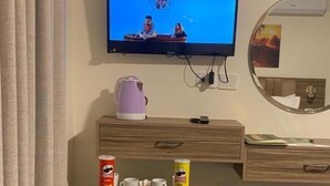 A hotel room with a television mounted on the wall, a small refrigerator with beverages, a kettle, and a cup of coffee on the counter. - Petra Jewel Hotel (Wadi Musa)