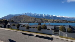A residential area with modern houses, a clear blue sky, and a mountain range with snow-capped peaks in the background.