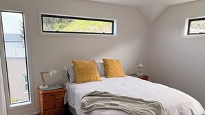 A bedroom with a bed, two bedside tables, a window, and a ceiling light.