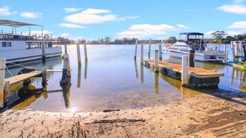 A calm waterfront with boats docked at wooden piers, a sandy shore, and a clear sky.