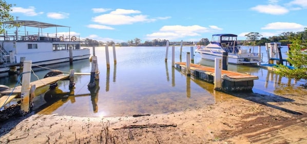 A calm waterfront with boats docked at wooden piers, a sandy shore, and a clear sky.