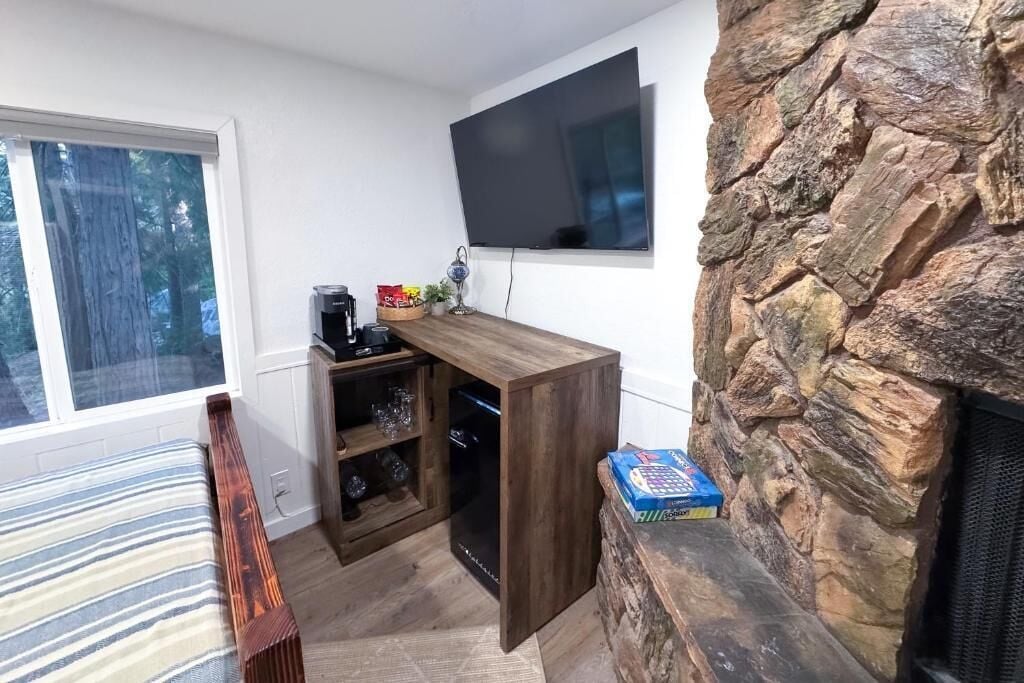 Une pièce chaleureuse avec un banc en bois, une cheminée en pierre, un téléviseur fixé à un mur blanc et une fenêtre donnant sur une forêt.