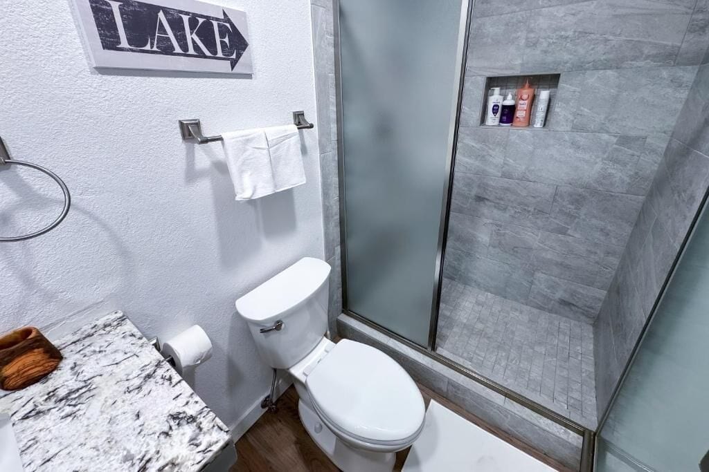 Un baño con inodoro, lavamanos de mármol, cabina de ducha de vidrio y un perchero para toallas.