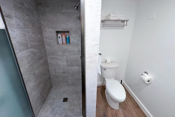 A bathroom with a shower, toilet, and a shelf with toiletries. - Arrowhead Ranch Retreat and Conference (Lake Arrowhead)