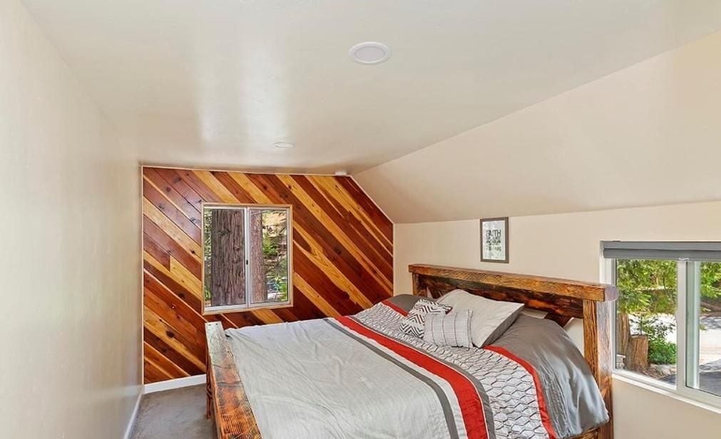 A bedroom with a sloped ceiling, a bed with a wooden headboard, a window, and a view of greenery outside.