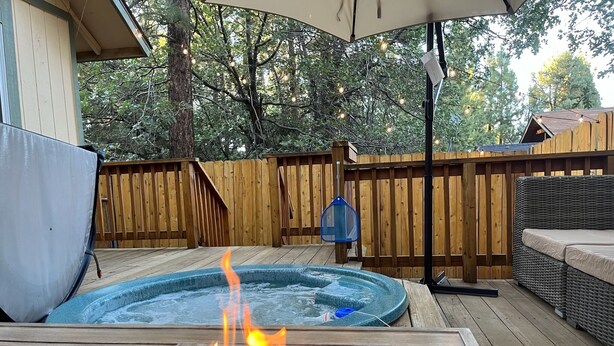A hot tub with a fire feature, surrounded by wooden deck and outdoor furniture.