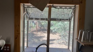 A kitchen with a window, a wooden cutting board, hanging wine glasses, and a metal rack.