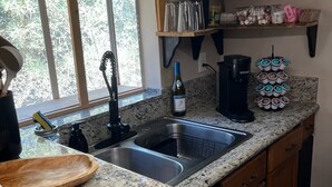 A kitchen with granite countertops, a double sink, a coffee maker, and a wine bottle.