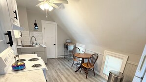 A compact kitchen with a white countertop, a stove, a ceiling fan, and a dining area with a table and chairs.