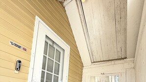 A porch with a white door, a bench, a welcome mat, and a 'No Smoking' sign.
