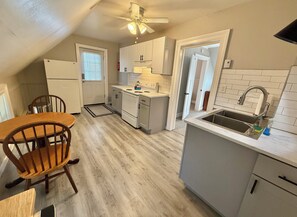 Une cuisine compacte avec un coin repas, des meubles blancs, un réfrigérateur, un évier et un ventilateur de plafond.