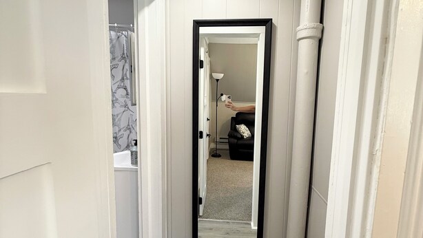A hallway with white walls, a black-framed mirror, and a light fixture on the ceiling.