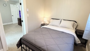 A bedroom with a bed, a nightstand, a lamp, a ceiling fan, and a door leading to another room.