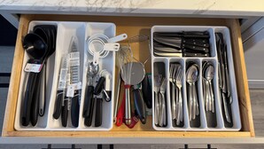A drawer with kitchen utensils and tools, including measuring cups, spoons, and knives.