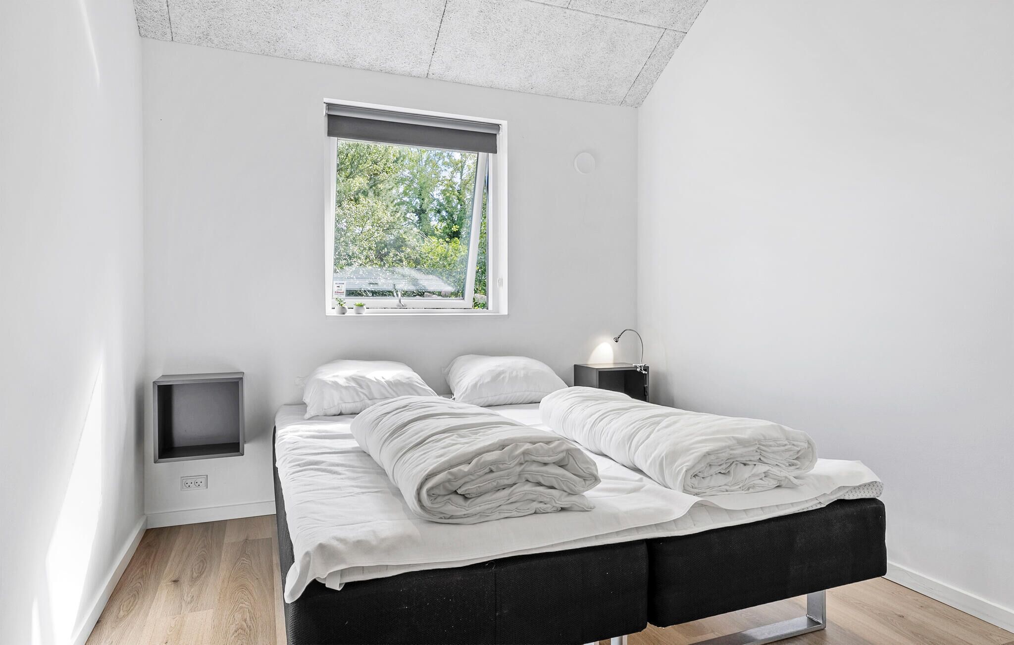 Una camera da letto moderna con un letto, comodini e una finestra vista verde.