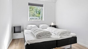 Une chambre moderne avec un lit, des tables de chevet et une fenêtre donnant sur un paysage verdoyant.