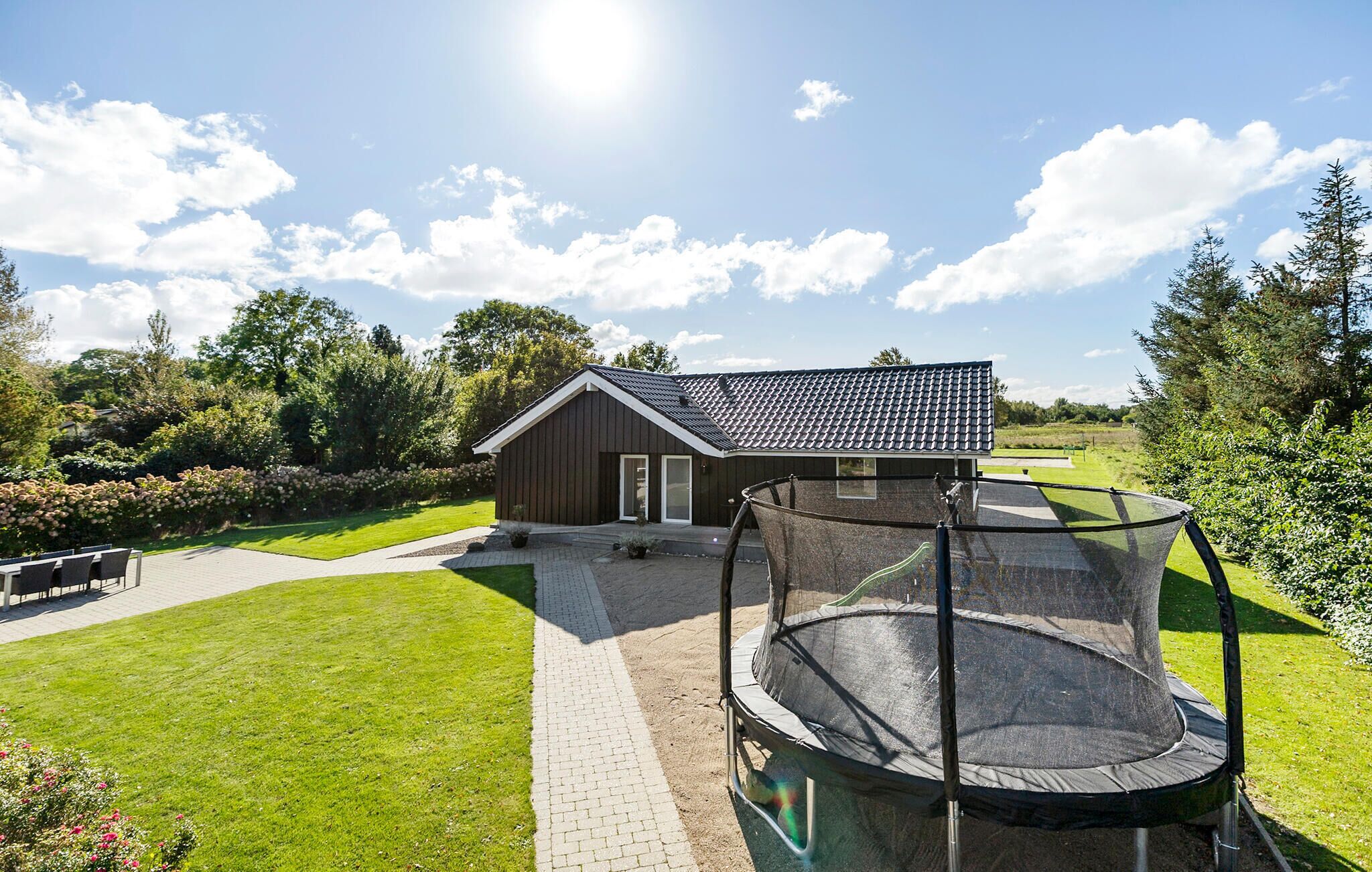 A house with a fenced backyard, a trampoline, and a paved patio area.