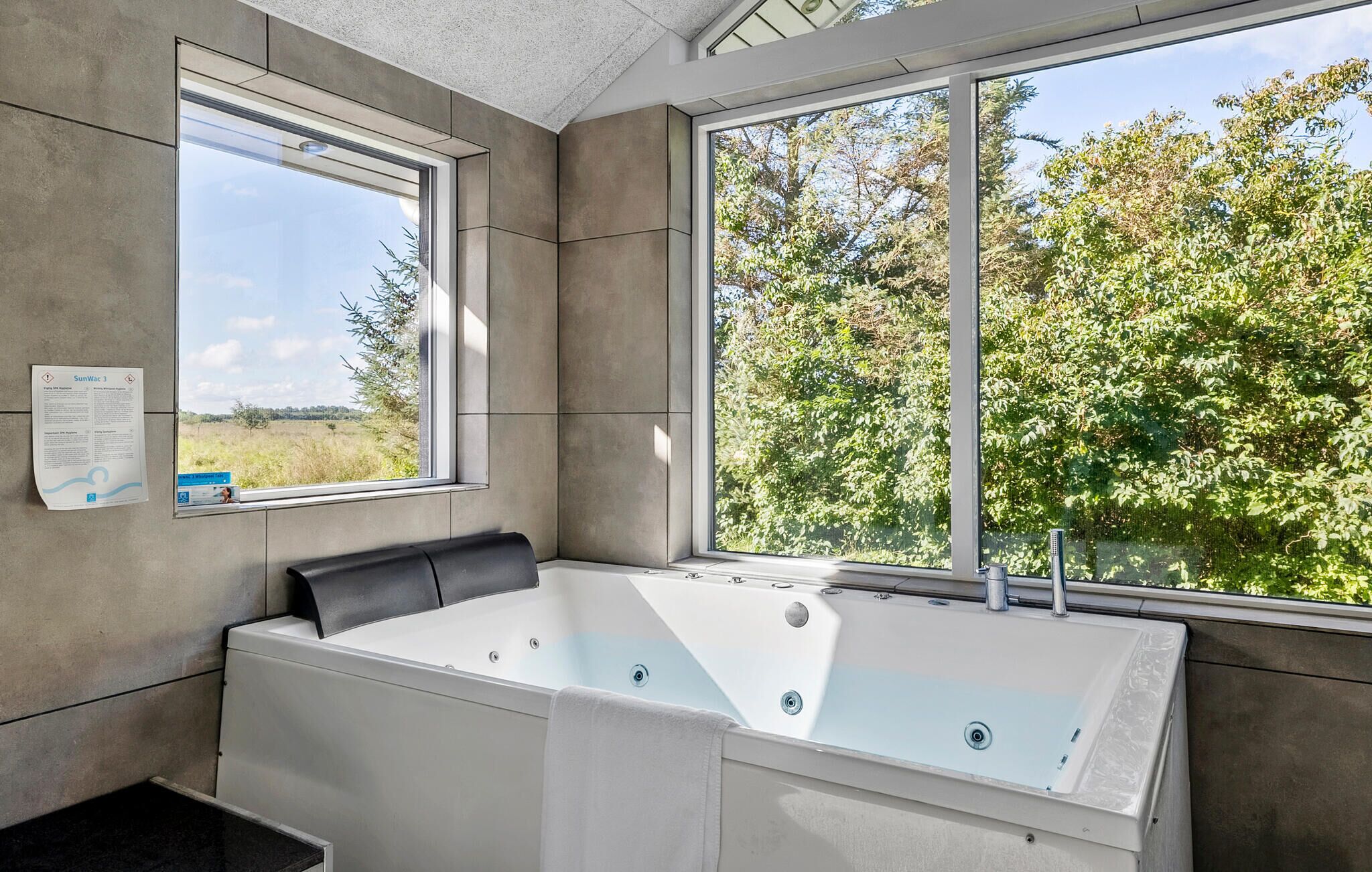 Une salle de bain moderne avec une grande baignoire, deux fenêtres et une vue sur la verdure.