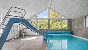 Une piscine intérieure avec un toboggan, une échelle et un espace détente près de la fenêtre.