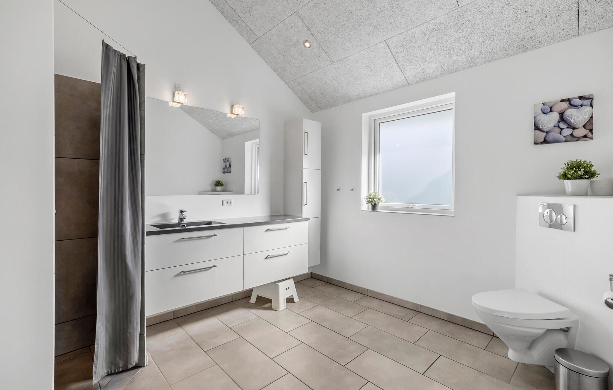 A modern bathroom with a large mirror, a vanity with a sink, a toilet, and a window.