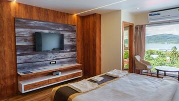 A modern hotel room with a large flat-screen TV mounted on a wooden wall, a bed with neatly folded towels, a small table, and a chair.