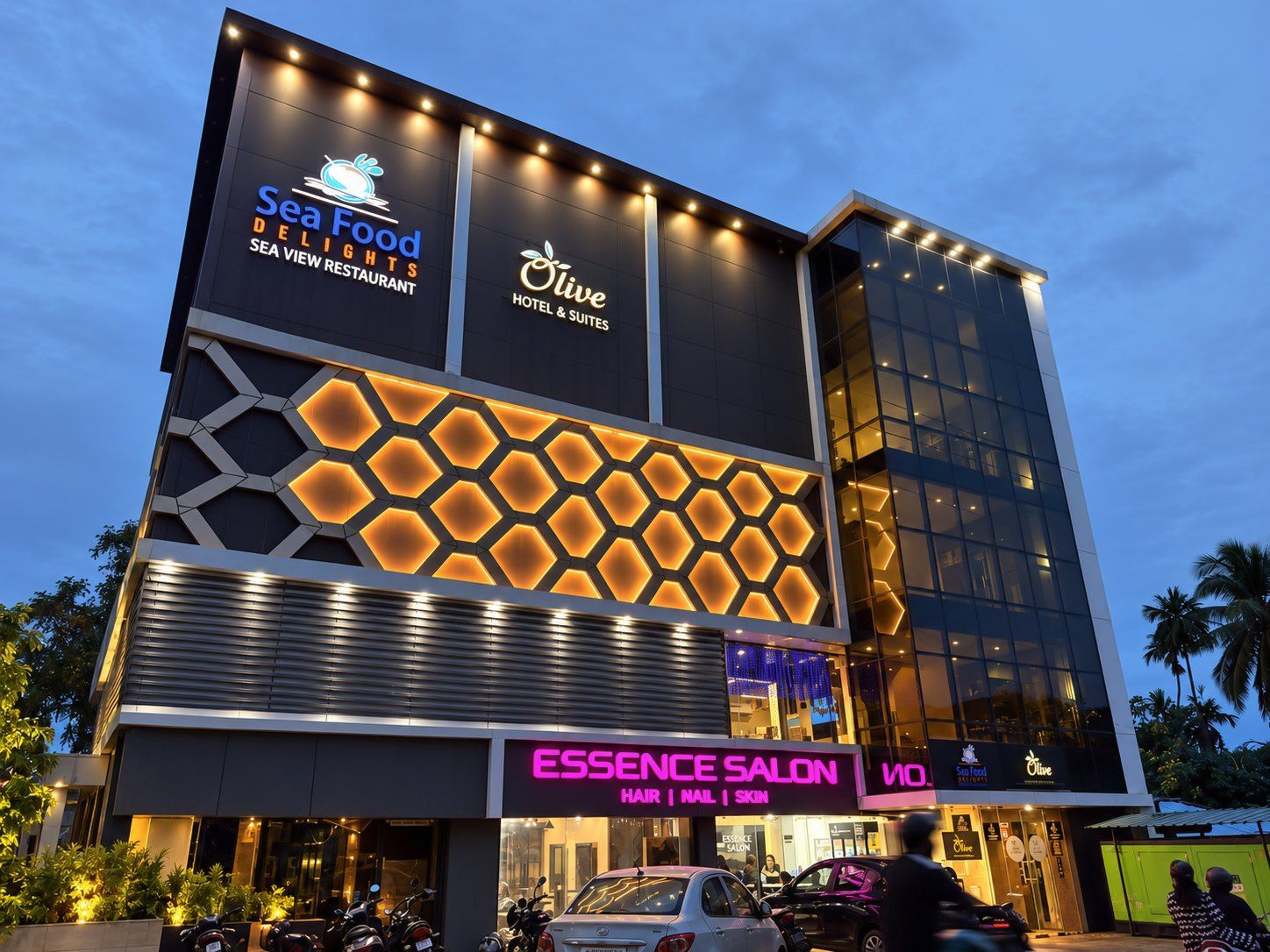 A multi-story building with signage for Sea Food DELIGHTS SEA VIEW RESTAURANT, Olive HOTEL & SUITES, and ESSENCE SALON offering hair, nail, and skin services.
