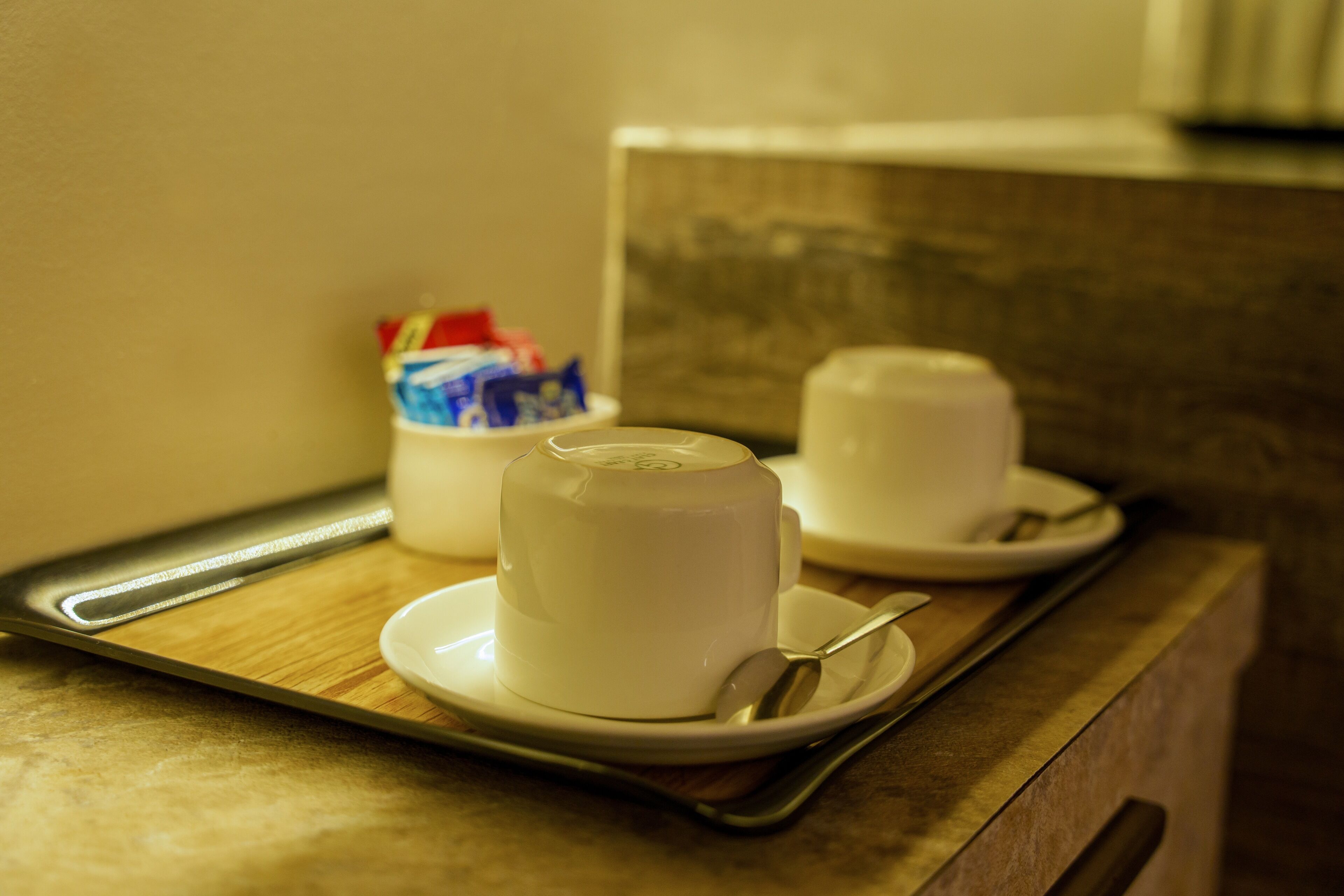 A tray with two white cups and a spoon on a wooden surface.