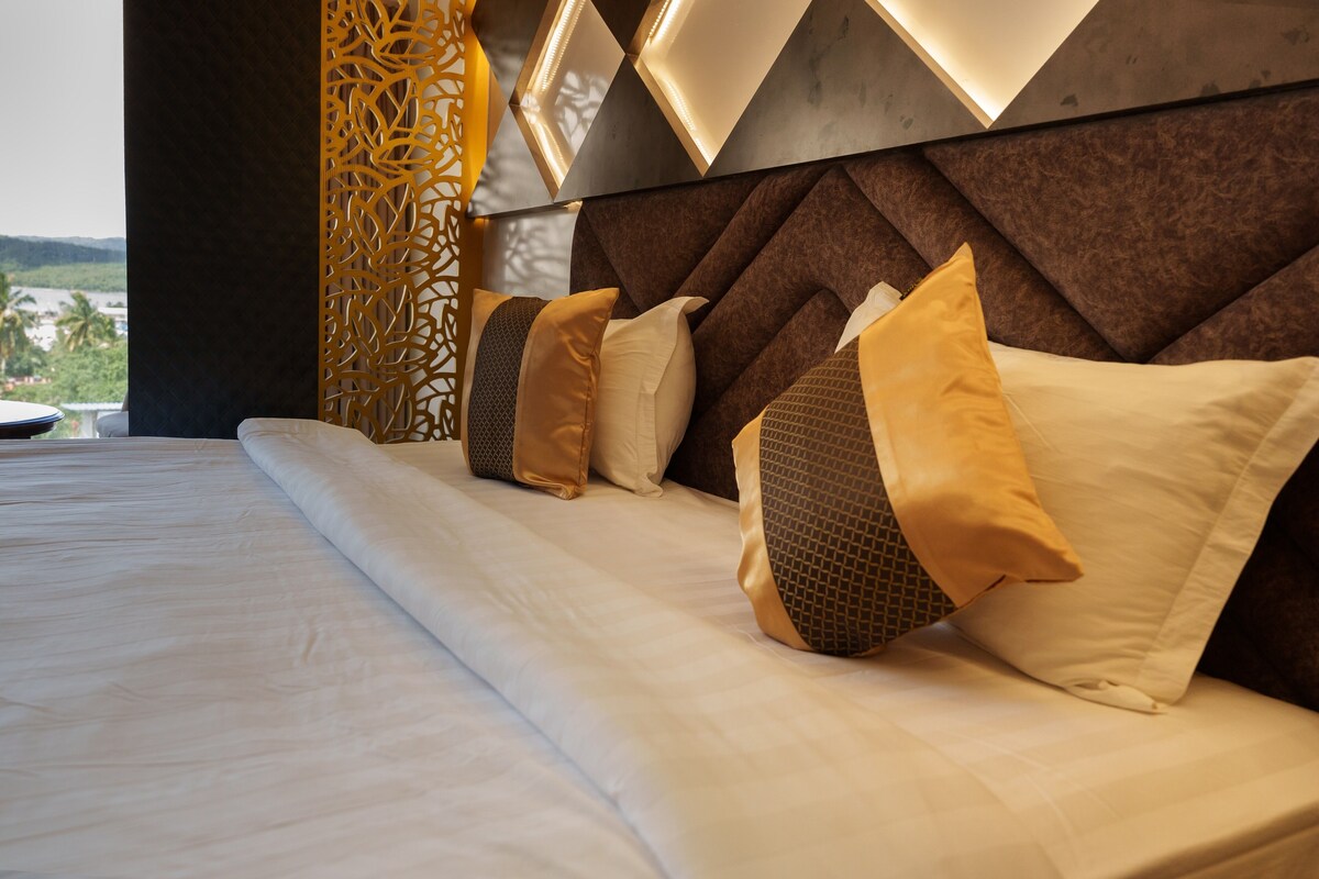 A neatly made bed with a headboard featuring geometric patterns and a view of a natural landscape through a window.