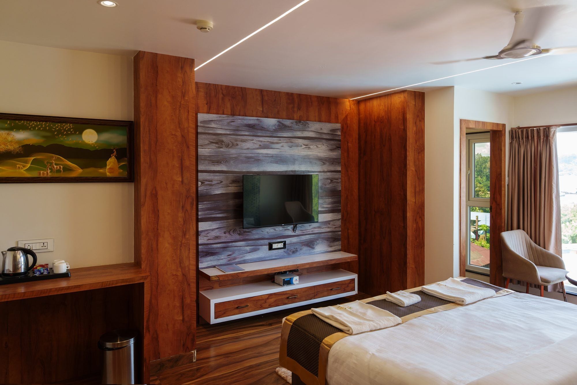 Habitación de hotel moderna con pared decorativa de madera, televisor de pantalla plana, cama, zona de estar y ventana con cortinas.