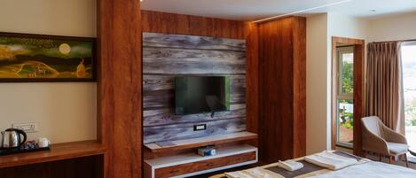 Habitación de hotel moderna con pared decorativa de madera, televisor de pantalla plana, cama, zona de estar y ventana con cortinas.
