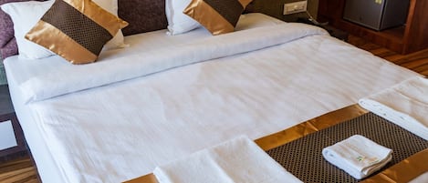 A double bed with a headboard, two pillows, a folded towel, and a small bedside table with a power outlet.