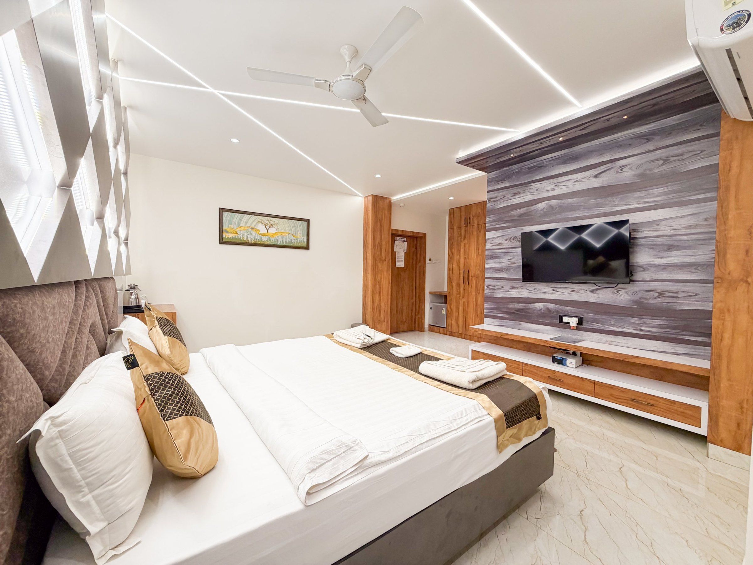 A modern hotel room with a bed, a TV mounted on a wooden wall, and a ceiling fan.