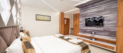 A modern hotel room with a bed, a TV mounted on a wooden wall, and a ceiling fan.