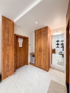 A hotel room with wooden wardrobes, a small refrigerator, and a bathroom with a geometric tile design. - Olive Hotel & Suites (Port Blair)