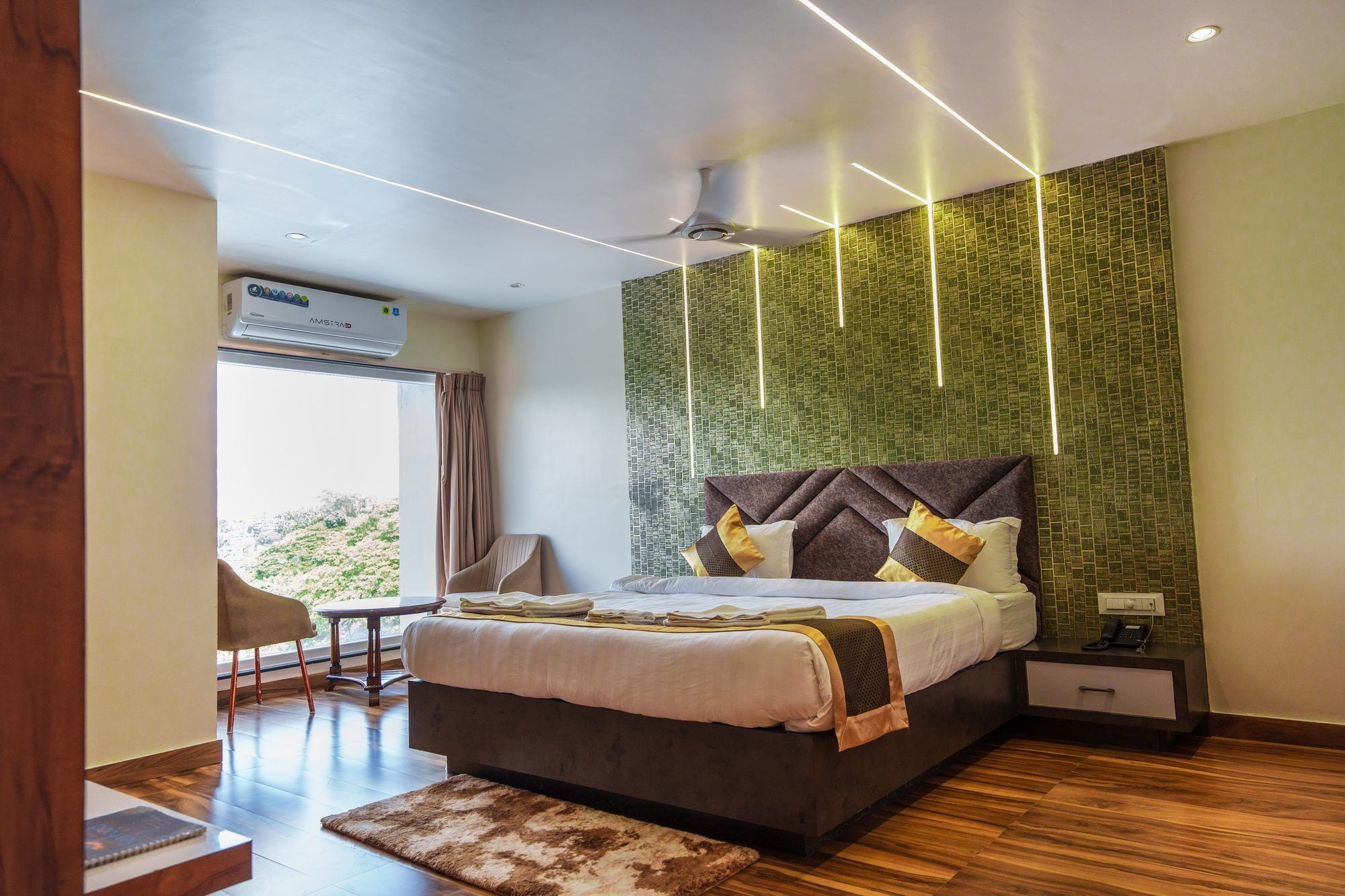 A modern hotel room with a large bed, a desk, and a view of greenery outside.
