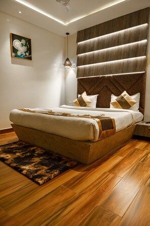 A modern bedroom with a large bed, a wooden headboard, and a decorative wall piece. - Olive Hotel & Suites (Port Blair)