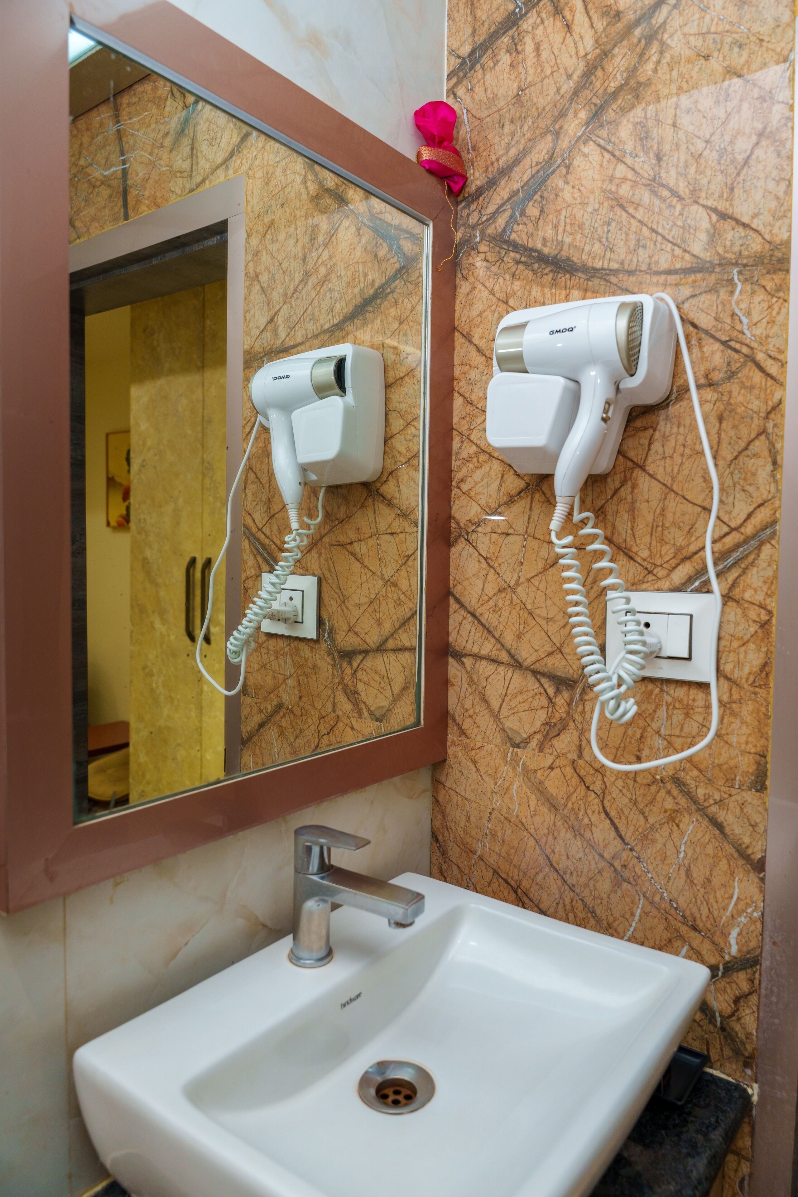 A bathroom with a sink, a mirror, and two hair dryers mounted on the wall.