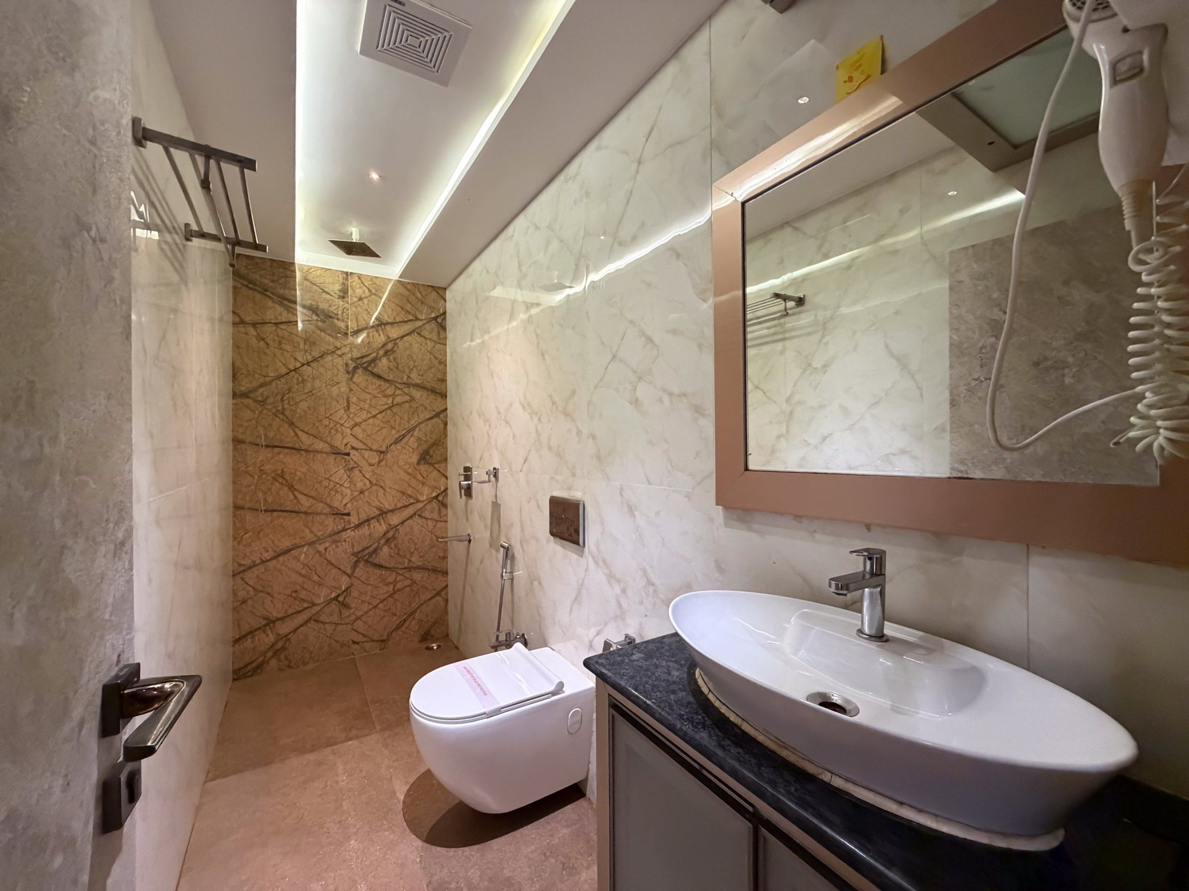 Ein modernes Badezimmer mit Marmorwand, Waschbecken in Weiß und einer Handbrause.