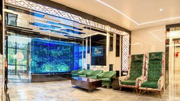A lobby with a reception desk, a large aquarium, green upholstered seating, and two ornate chairs.