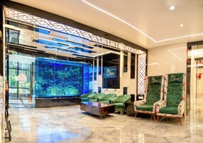 A lobby with a reception desk, a large aquarium, green upholstered seating, and two ornate chairs.