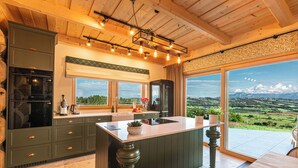 A modern kitchen with a large island, wooden ceiling beams, and a view of a green landscape through large windows. - Exclusive Villa for Family, Friends & Workation (Biały Dunajec)