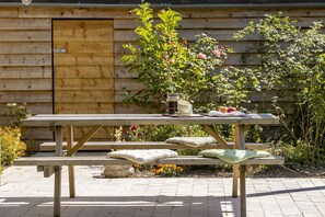 A wooden picnic table with benches, a small stone table, and a bench with cushions.