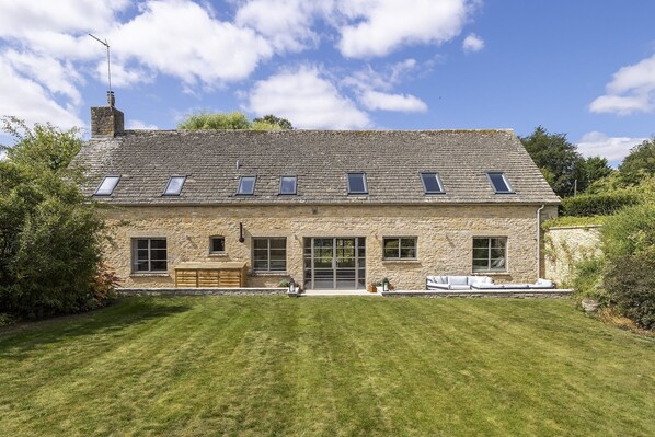 A stone house with a sloped roof, multiple windows, and a well-maintained lawn.