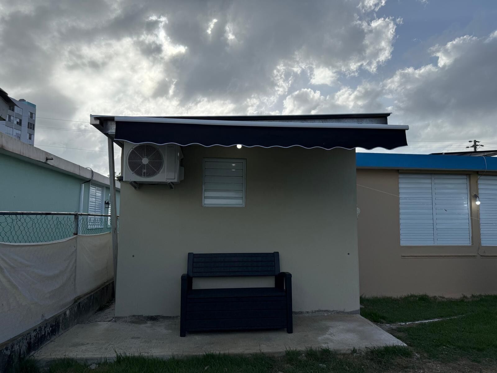 A small, single-story building with a sloped roof, a single window, and a wall-mounted air conditioning unit.