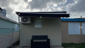 A small, single-story building with a sloped roof, a single window, and a wall-mounted air conditioning unit.