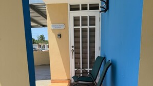 A covered outdoor seating area with two green chairs, a wooden floor, and a door labeled "Colombiano Baricua Apartment". - Colombian Boricua Apartment 5 minutes from the beach luxury (Quebradillas)