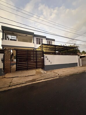 A modern two-story house with a gated entrance, a covered driveway, and a visible number on the wall. - 3-bedroom house in enjoyable Sabana Hoyos with AC (Sabana Hoyos)
