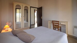 Um quarto com uma cama, uma escrivaninha, uma cadeira, um abajur e um guarda-roupa.