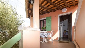 Varanda com mesa e cadeiras, teto de madeira e porta de acesso ao interior.