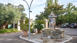 Uma rotatória com uma fonte central, rodeada por estruturas de pedra e plantas em vasos.